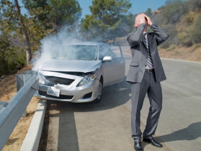 Frustrated businessman standing next to car wrecked on guardrail