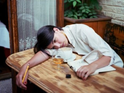 Young woman with notebook laying head on table (focus on face)