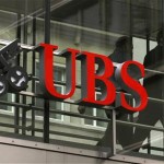 People walk behind the logo of Swiss bank UBS in Zurich