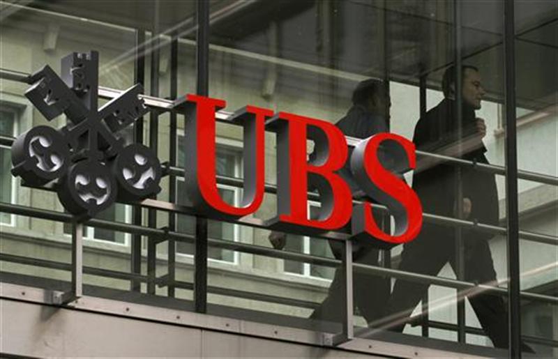 People walk behind the logo of Swiss bank UBS in Zurich