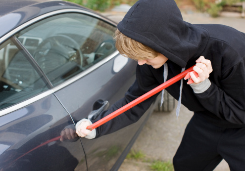 Burglar prying car window open with crowbar