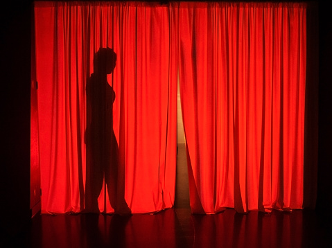 Female silhouette behind theatrical red curtains