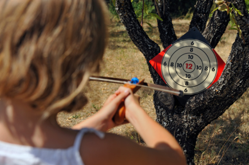 Girl aiming a target with crossbow, in garden