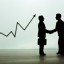 businessmen figurines shaking hands, graph in background.