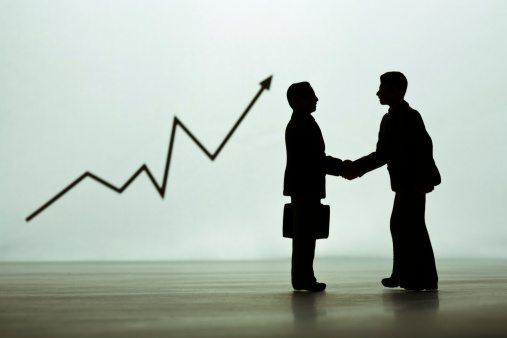 businessmen figurines shaking hands, graph in background.