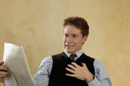 Businessman looking shocked while reading a newspaper