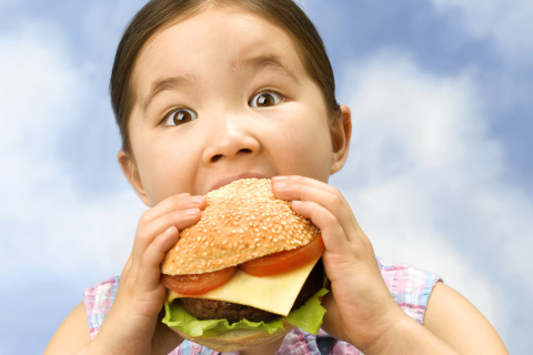 Little girl munching on a large burger