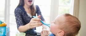 Girl feeding baby brother at table