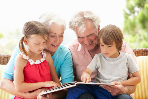 Grandparents And Grandchildren Reading Book On Garden Seat