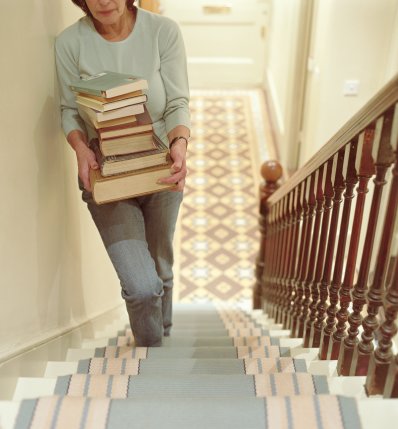 Mature woman ascending staircase, carrying pile of books