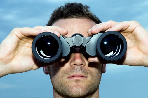 Man looking through binoculars outdoors, close-up